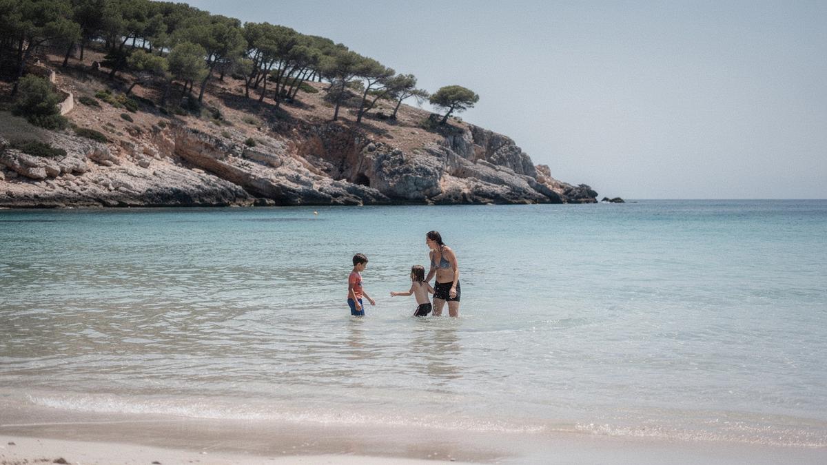 Two children wading on a wide, very shallow beach shelf in clear pale water, pine covered slope behind